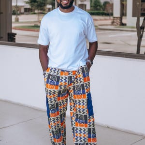 Puede incluir: Una camiseta blanca lisa de manga corta combinada con pantalones holgados que presentan un vibrante patrón geométrico en tonos naranja, azul, negro y blanco. Los pantalones incluyen bolsillos cargo laterales en azul sólido y corte recto.