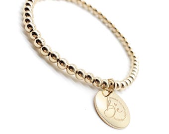 May include: Gold beaded bracelet with a round charm. The charm is engraved with the word "Be" and the words "Strong, Confident, Positive". The bracelet is on a white background.