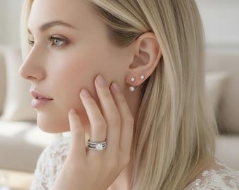 May include: A silver-toned ring featuring a central round-cut stone set on a multi-band shank, paired with double-sided earrings consisting of a small stud and a larger pearl-like sphere that sits behind the earlobe, creating a layered appearance.