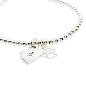 May include: A silver beaded bracelet with a heart charm engraved with the letter "L" and a paw print charm.