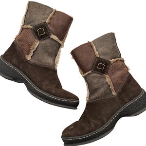 以下が含まれることがあります： パッチワークデザインの茶色のスエードブーツのペア。ブーツは、濃い茶色のソール、正方形のバックルディテール、フェイクファートリムが特徴です。ブーツの高さは約20cmです。