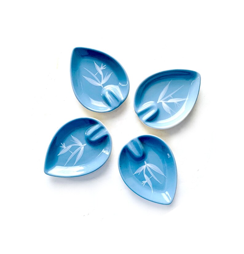 May include: Four blue ceramic ashtrays with white floral designs. The ashtrays are shaped like teardrops and have a small indentation for cigarettes.