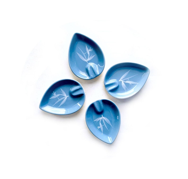 May include: Set of four blue ceramic ashtrays with a white floral design. Each ashtray is shaped like a teardrop.