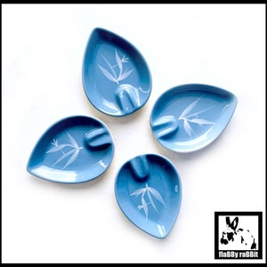 May include: Four blue ceramic ashtrays with a white floral design. Each ashtray has a unique design and is shaped like a teardrop.