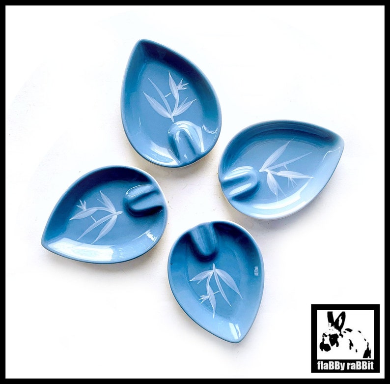 May include: Four blue ceramic ashtrays with a white floral design. Each ashtray has a unique design and is shaped like a teardrop.