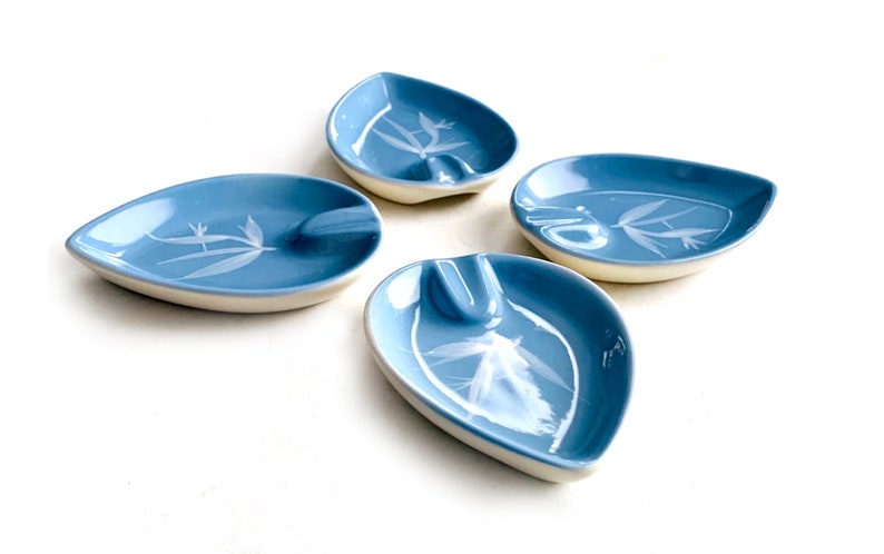May include: Set of four blue ceramic leaf-shaped ashtrays with white floral designs.