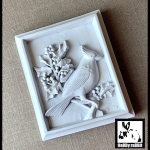 Puede incluir: Decoraci&oacute;n de pared enmarcada en blanco con una escultura en relieve 3D de un cardenal posado en una rama de acebo con bayas rojas. La escultura est&aacute; firmada "D 79".