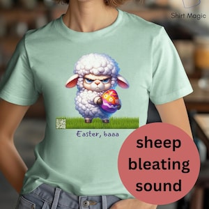 Könnte beinhalten: Ein hellblaues T-Shirt mit einem Cartoon-Bild eines weißen Schafes, das ein buntes Osterei hält. Der Text "Easter, baaa" ist unter dem Bild gedruckt.