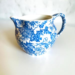 Könnte beinhalten: Ein Set aus drei Keramikbechern mit gesprenkelter, matter Oberfläche. Jeder Becher hat eine andere Farbe: hellblau, cremefarben und grau. Die Becher haben ein schlichtes, modernes Design mit runder Form und Henkel.