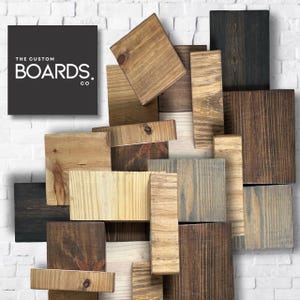 Op de afbeelding: Een verzameling gerecyclede houten planken in verschillende tinten bruin, grijs en natuurlijk hout. De planken zijn in een willekeurig patroon gerangschikt, wat een unieke en rustieke uitstraling cre&euml;ert. De tekst "THE CUSTOM BOARDS. CO" is zichtbaar in de linkerbovenhoek van de afbeelding.