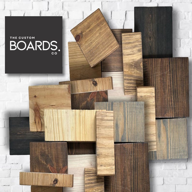 Op de afbeelding: Een verzameling gerecyclede houten planken in verschillende tinten bruin, grijs en natuurlijk hout. De planken zijn in een willekeurig patroon gerangschikt, wat een unieke en rustieke uitstraling cre&euml;ert. De tekst "THE CUSTOM BOARDS. CO" is zichtbaar in de linkerbovenhoek van de afbeelding.