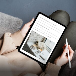 Könnte beinhalten: Ein schwarzes Tablet mit Text und einem Bild einer gemütlichen Szene mit Kaffeetassen und einem gestrickten Gegenstand. Der Text enthält Aufforderungen wie „Ich werde mich mit jemandem verbinden“ und „Sie müssen nicht alles tun“. Ein weißer Stift wird in der Nähe gehalten.