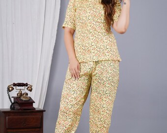 May include: Yellow floral print pyjama set. The set includes a short-sleeved top and matching trousers. The pyjamas have a light yellow background with a pattern of small red and green dots. The model is wearing beige sandals.