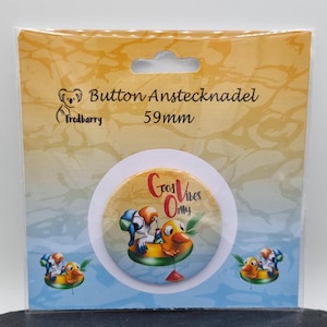 Könnte beinhalten: Ein 59 mm Knopf mit einer Cartoon-Illustration von zwei Vögeln auf einer gelben Gummi-Ente mit dem Text "Good Vibes Only". Der Knopf befindet sich auf einem weißen Hintergrund mit einem blauen und gelben Rand.