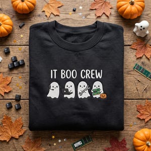 Könnte beinhalten: Ein schwarzes Sweatshirt mit Rundhalsausschnitt und dem weißen Schriftzug IT BOO CREW über vier gezeichneten Geistern. Der erste Geist trägt ein Headset, der zweite nutzt einen Laptop, der dritte hält einen Schraubenschlüssel und der vierte eine Platine.