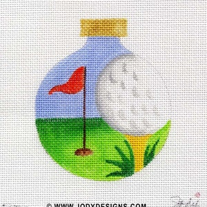 May include: A white golf ball on a green golf course with a red flag and a yellow tee. The golf ball is inside a blue and white Christmas ornament with a gold top.