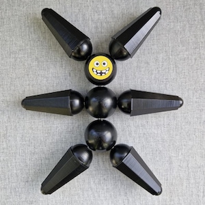May include: A black articulated toy figure with six limbs and a yellow smiley face sticker on the torso.