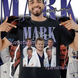 May include: Black t-shirt featuring a collage of images of Mark Sloan, with the name "Mark Sloan" in a purple font. The shirt has a vintage, retro design with a lightning bolt background.