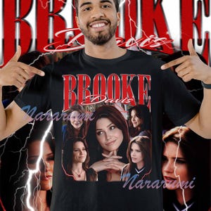 May include: Black t-shirt featuring a collage of images and the name "Brooke Davis" in red. The design includes a signature and lightning bolt graphics, creating a vintage aesthetic.