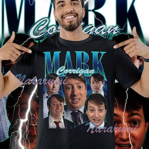 Peut inclure: T-shirt noir avec le nom "MARK Corrigan" en bleu sarcelle et blanc. Le t-shirt présente un collage d'images d'un homme. Le fond a un design bleu et blanc avec des éclairs.