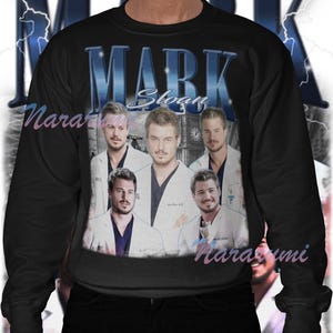 Puede incluir: Sudadera negra con un collage de im&aacute;genes de un hombre con bata blanca, y el nombre "MARK Sloan" en letras azules. La sudadera tiene un estilo vintage con un dise&ntilde;o de rayo.
