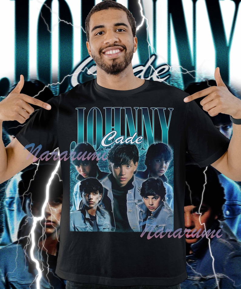 May include: Black t-shirt featuring a teal and white graphic of the name "JOHNNY Cade" above a collage of five images of a person wearing a denim jacket. The background has a teal and white lightning bolt design.