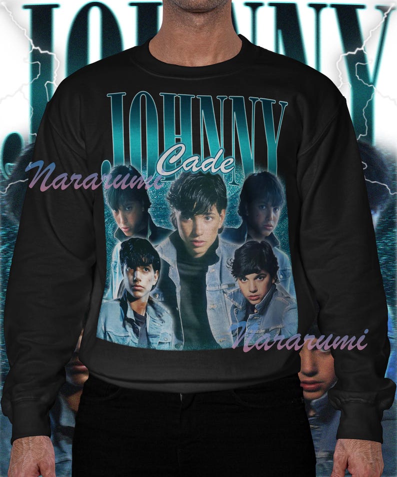 May include: Black sweatshirt featuring a teal and white graphic with the text "JOHNNY Cade" and images of a young man. The design has a vintage, retro aesthetic. The sweatshirt is a crew neck style.
