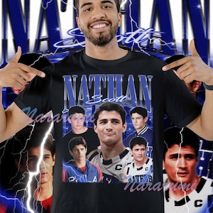 May include: Black t-shirt featuring the name "Nathan Scott" in blue, along with multiple images of a man. The design includes a blue lightning bolt effect and the word "Scott" in a stylized font.