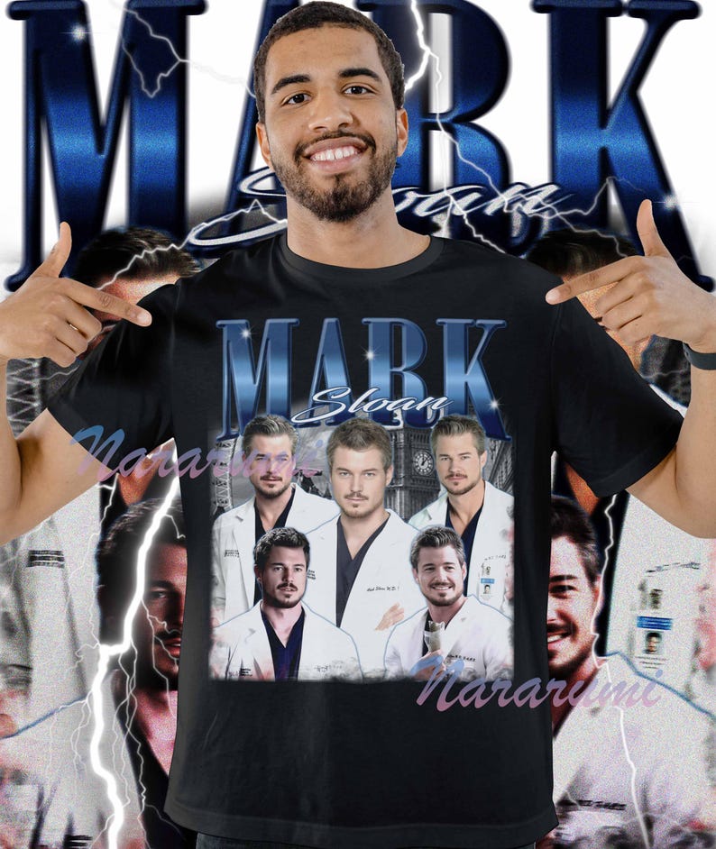 Puede incluir: Camiseta negra con texto "MARK Sloan" en azul estilizado e im&aacute;genes de actores con batas blancas. El dise&ntilde;o incluye un fondo azul con rayos. La camiseta es de cuello redondo.