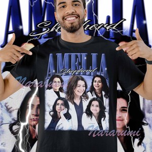 Może przedstawiać: Czarna koszulka z napisem "AMELIA Shepherd" w niebieskim, w stylu vintage. Koszulka przedstawia kolaż zdjęć kobiet. Tło ma niebieski wzór błyskawicy.