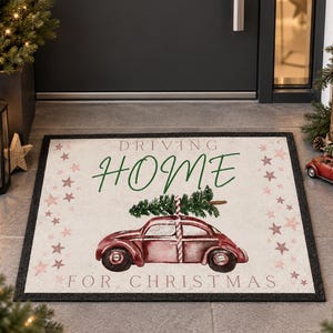 Könnte beinhalten: Eine rechteckige Fußmatte mit hellem Hintergrund, die ein rotes Oldtimer-Auto mit einem grünen Weihnachtsbaum auf dem Dach zeigt. Der Text DRIVING HOME FOR CHRISTMAS ist in grüner und schwarzer Schrift gedruckt und von kleinen rosa Sternen umgeben.