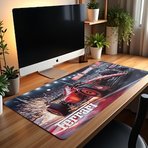 May include: A rectangular desk mat featuring a red Ferrari Formula 1 race car in motion. The mat has a black background with sparks and the Ferrari logo in white. A computer monitor sits above the mat.