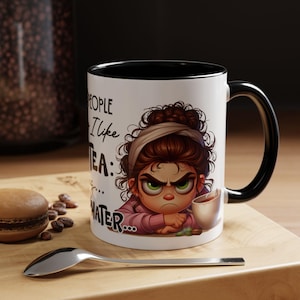 Puede incluir: Taza de cerámica blanca con interior y asa negros. La taza presenta una ilustración de dibujos animados de una mujer enfadada con el texto "...PEOPLE I like TEA: ... WATER...". Una cuchara y un macaron están en primer plano.