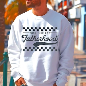 Puede incluir: Sudadera blanca con un patrón de cuadros blanco y negro y el texto "Mind Your Own Fatherhood" en una fuente retro.