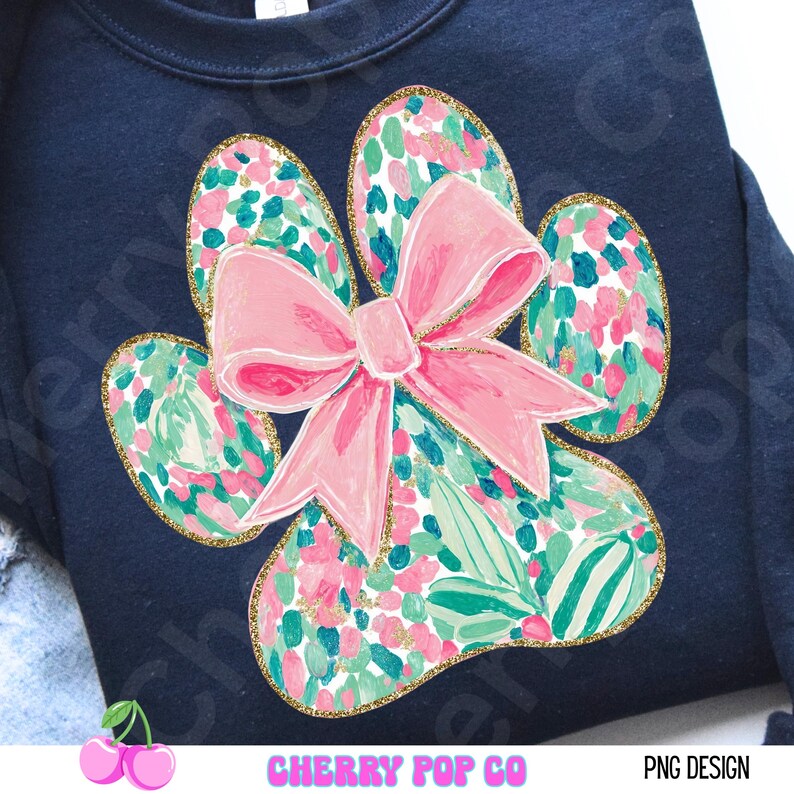 Puede incluir: Sudadera azul marino con un dise&ntilde;o de gran huella de pata y un lazo rosa. La huella de la pata est&aacute; llena de un estampado floral en rosa, verde y blanco, delineado con purpurina dorada. El texto "CHERRY POP CO" y "PNG DESIGN" est&aacute; en la parte inferior.
