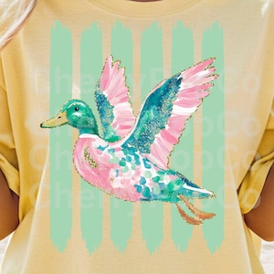 K&ouml;nnte beinhalten: Ein gelbes T-Shirt mit einem farbenfrohen Enten-Design. Die Ente hat rosa und t&uuml;rkisfarbene Fl&uuml;gel mit goldenen Glitzerakzenten, einen gr&uuml;nen Kopf und einen rosa und t&uuml;rkisfarbenen K&ouml;rper. Vertikale hellgr&uuml;ne Pinselstriche befinden sich hinter der Ente.