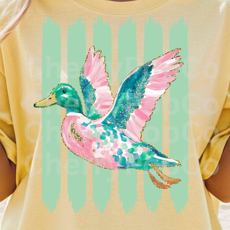 K&ouml;nnte beinhalten: Ein gelbes T-Shirt mit einem farbenfrohen Enten-Design. Die Ente hat rosa und t&uuml;rkisfarbene Fl&uuml;gel mit goldenen Glitzerakzenten, einen gr&uuml;nen Kopf und einen rosa und t&uuml;rkisfarbenen K&ouml;rper. Vertikale hellgr&uuml;ne Pinselstriche befinden sich hinter der Ente.