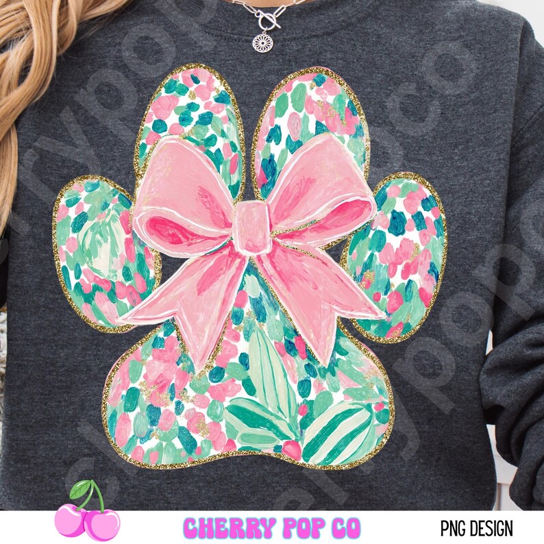 Puede incluir: Sudadera gris oscuro con un dise&ntilde;o de huella de pata grande y un lazo rosa. La huella de la pata est&aacute; llena de un estampado floral en rosa, verde y dorado. El texto "CHERRY POP CO" est&aacute; en la parte inferior.