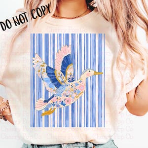 May include: A white t-shirt featuring a colorful duck design with blue, pink, and floral patterns. The duck is set against a blue and white striped background. The text "DO NOT COPY" is in the upper left corner.