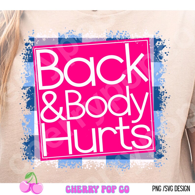 May include: A beige t-shirt featuring a pink square with the words "Back & Body Hurts" in white. The square is set against a blue and white plaid background with blue paint splatters. The Cherry Pop Co logo is at the bottom.