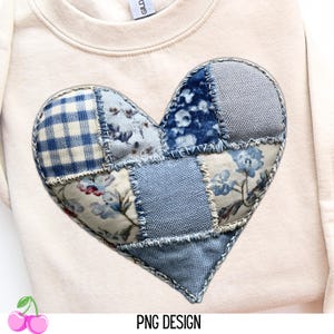 May include: Cream-colored sweatshirt with a large, patchwork heart design. The heart is composed of various blue fabrics, including floral prints, denim, and gingham. The design is stitched onto the sweatshirt. The text "PNG DESIGN" is at the bottom.
