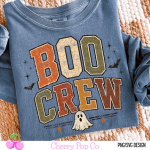 May include: A blue long-sleeve t-shirt featuring the text BOO CREW in distressed orange, green, and brown block letters. The design includes small black bat silhouettes, star shapes, and a white ghost illustration at the bottom center.