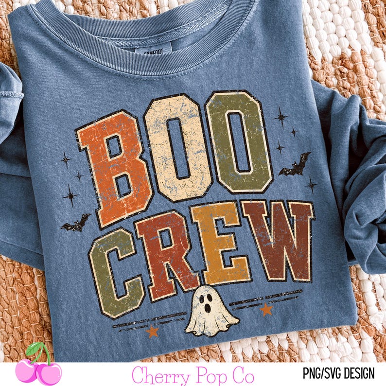 May include: A blue long-sleeve t-shirt featuring the text BOO CREW in distressed orange, green, and brown block letters. The design includes small black bat silhouettes, star shapes, and a white ghost illustration at the bottom center.