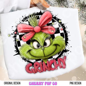 May include: A white graphic featuring a green Grinch character with a pink bow and the word "Grinchy" in pink. The Grinch is set against a black and white checkered background with a black splatter effect.