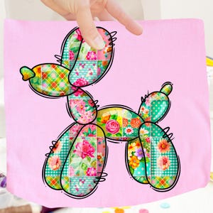 May include: A colorful balloon dog design on a pink background. The dog is composed of patchwork patterns featuring floral, polka dot, and plaid designs in various colors. The balloon dog is held by a hand.