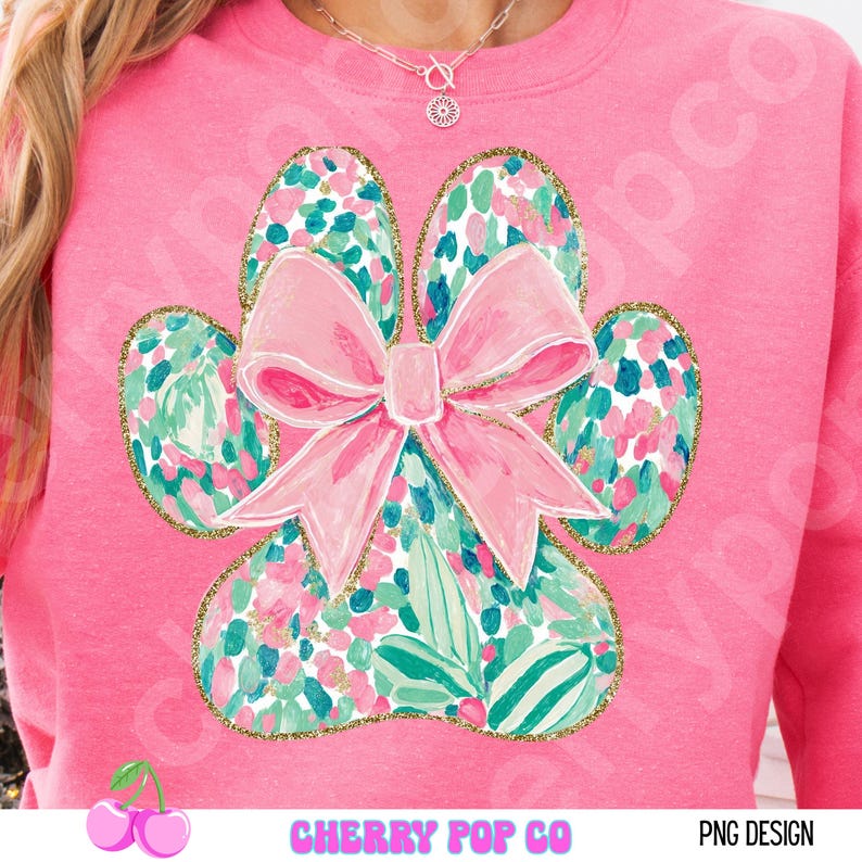 Puede incluir: Sudadera rosa con un dise&ntilde;o de huella de pata grande y un lazo rosa. La huella de la pata est&aacute; llena de un estampado floral en rosa, verde y dorado. El texto "CHERRY POP CO" est&aacute; en la parte inferior.