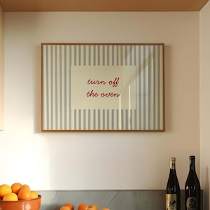 Puede incluir: Escena de cocina con un cuadro enmarcado que dice "turn off the oven". Un cuenco de terracota lleno de naranjas se encuentra sobre una encimera de mármol, junto con varias naranjas sueltas. También hay dos botellas de vino.