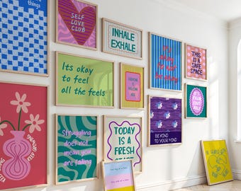 May include: A collection of framed art prints with inspirational quotes and colorful designs. The prints feature phrases like "Self Love Club," "Inhale Exhale," and "Today is a Fresh Start." The artwork is displayed on a white wall, creating a gallery-like atmosphere.