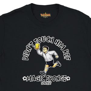 May include: Black t-shirt with a cartoon illustration of a soccer referee holding a yellow sponge, with the text "DIDN'T TOUCH HIM REF" above and "MAGIC SPONGE SORTED!" below. The shirt has a crew neck and short sleeves.