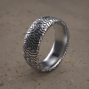 Può includere: Un anello d'argento con un design testurizzato e a motivi. L'anello è contrassegnato con "925" all'interno.